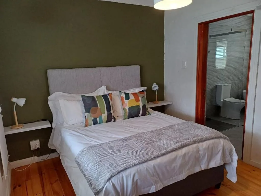 Modern bedroom with queen bed, colorful pillows, olive green accent wall, and ensuite bathroom