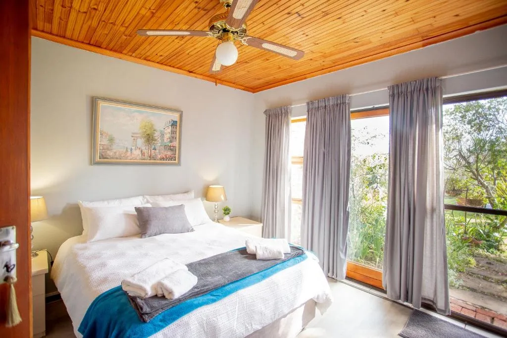 Bright bedroom with wooden ceiling, queen bed, garden views through glass doors