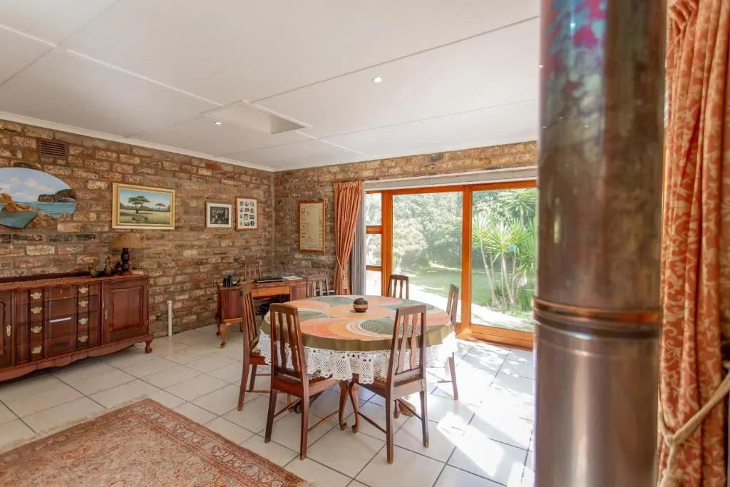 Dining room with round table, wooden chairs, brick walls, and garden views