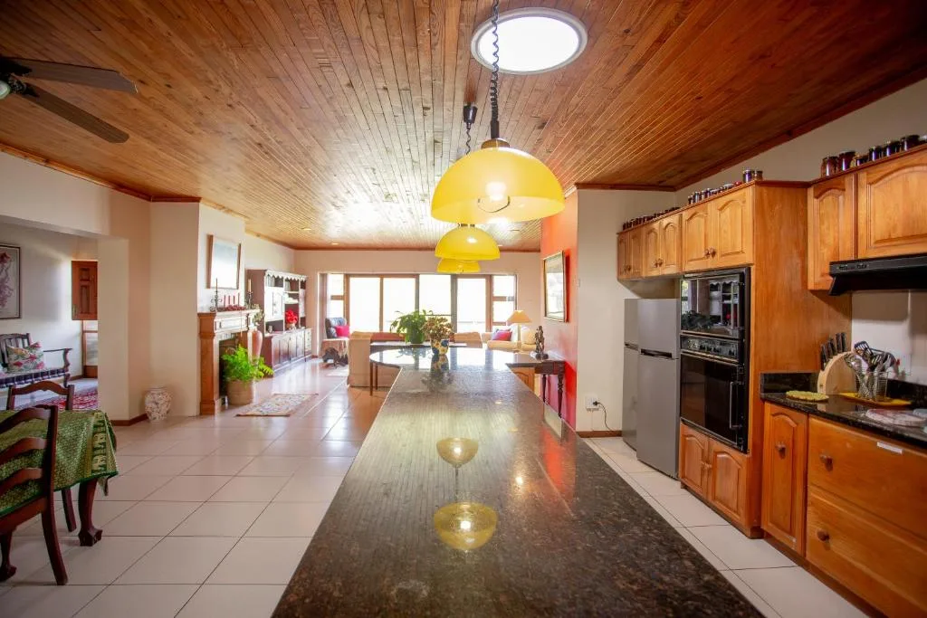 Open-plan kitchen with wooden cabinetry, stainless steel appliances, and yellow pendant lights