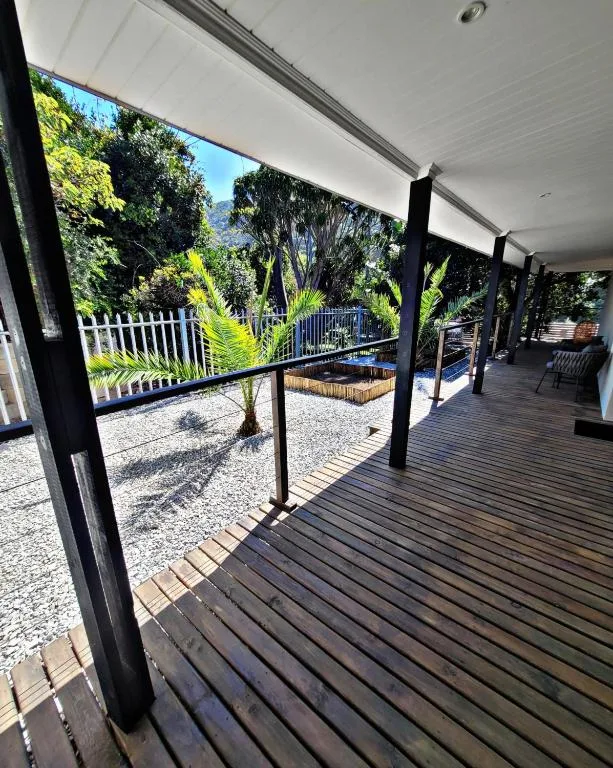 Covered wooden deck with black railings overlooking lush gardens and landscaping
