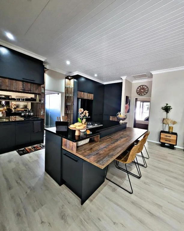 Modern black kitchen with island counter, wooden accents, and dining chairs
