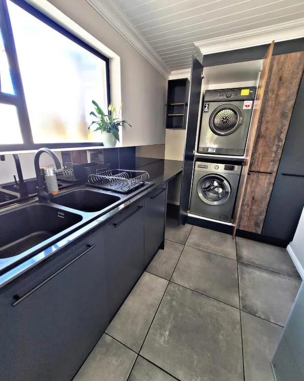 Modern kitchen with black cabinetry, sink, and stacked washer-dryer units