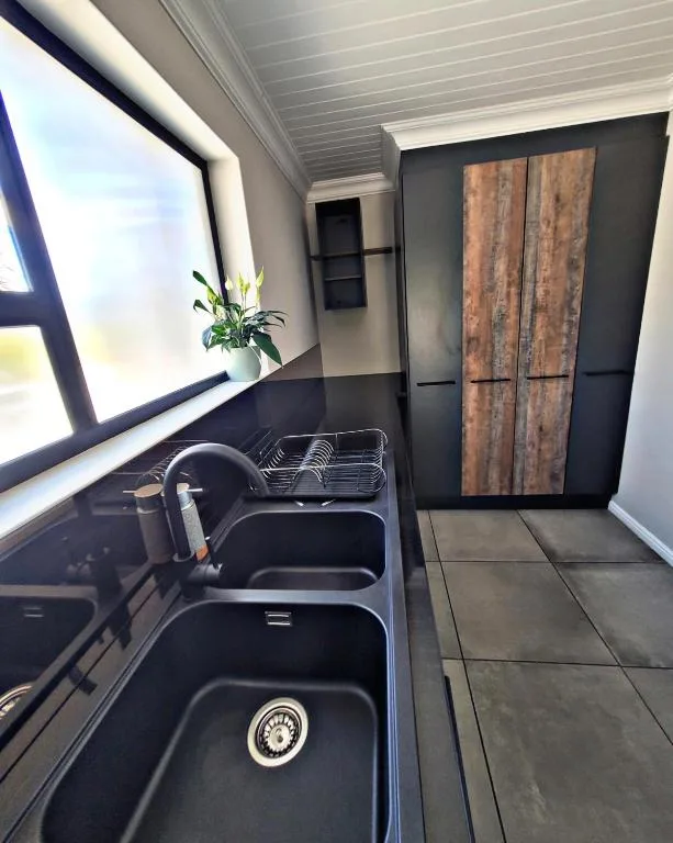 Modern kitchen with black sink, window view, and wooden wardrobe doors