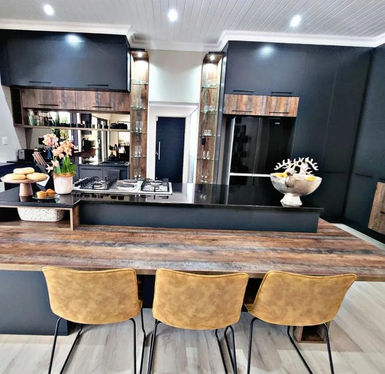 Modern kitchen with black cabinetry, wooden countertop, and gold bar stools