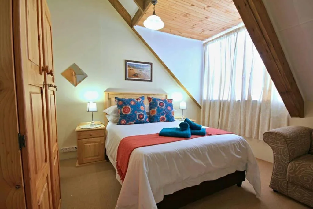 Bright loft bedroom with wooden beams, colorful pillows, and natural light