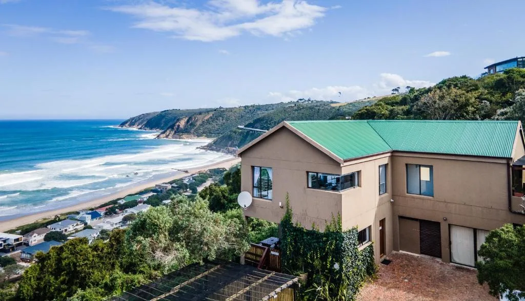 Beige house with green roof overlooking pristine beach and ocean cliffs