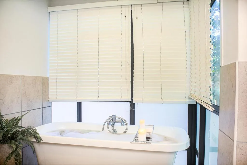 Modern bathtub with chrome faucet and white shutters overhead