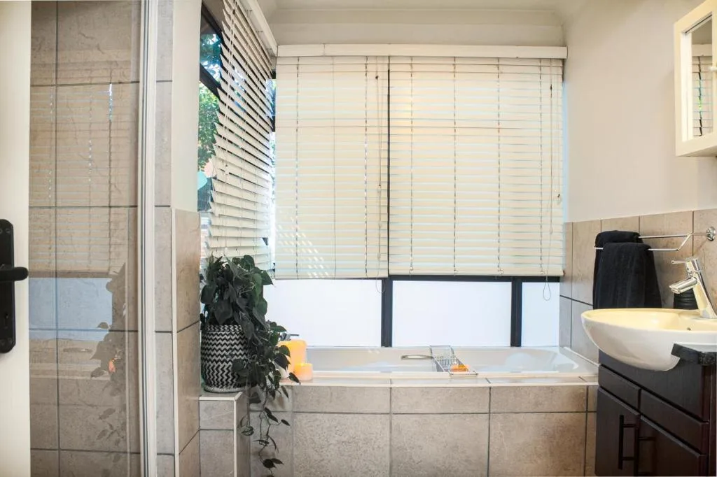 Bright bathroom with bathtub, shower enclosure, and window with shutters