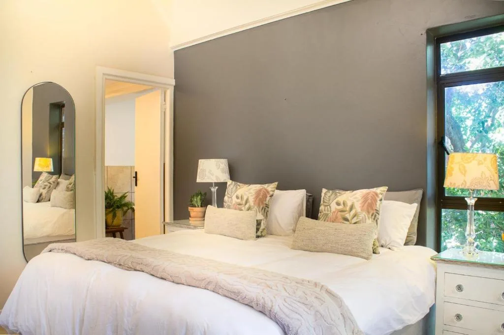 Bright bedroom with queen bed, decorative pillows, and garden views through windows