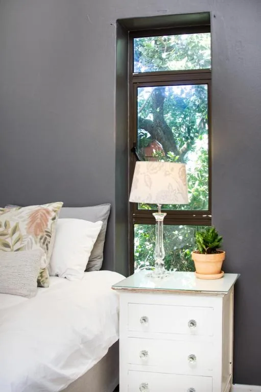 Bright bedroom with white bedside table, lamp, and garden views through tall window