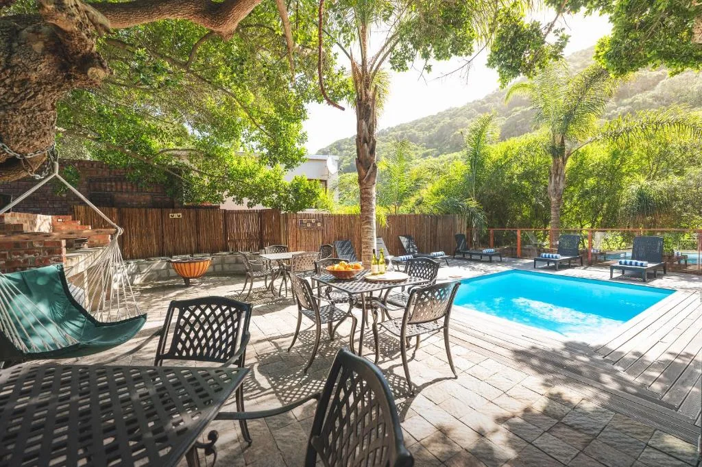 Swimming pool with loungers and dining area surrounded by lush green mountains