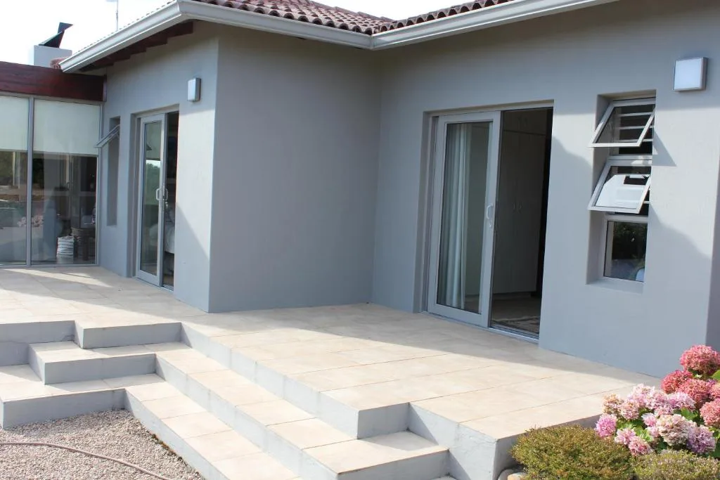 Modern white holiday home with paved patio, flowering plants, and glass doors