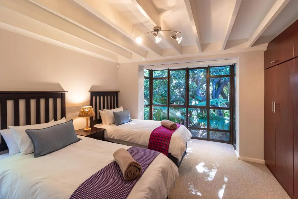Spacious bedroom with twin beds, large windows overlooking trees, and modern ceiling