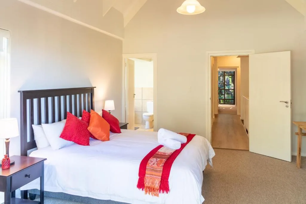 Spacious bedroom with dark wooden bed, red accent pillows, and en-suite bathroom access