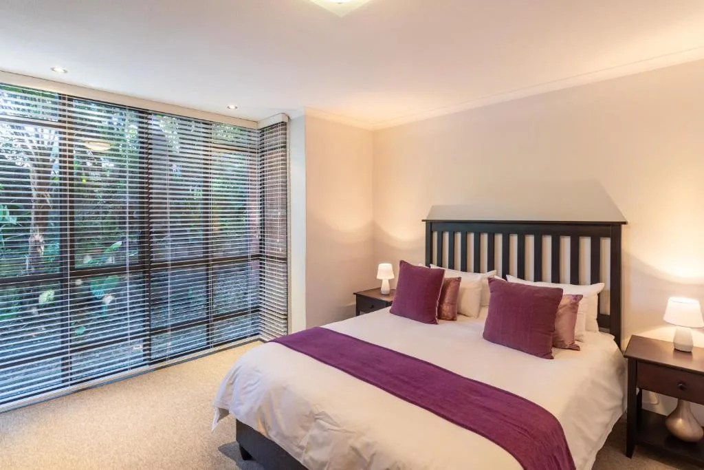 Spacious bedroom with queen bed, purple accents, and garden views through shutters