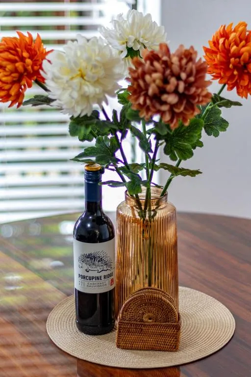 Colorful dahlia flowers in gold vase with wine bottle on table
