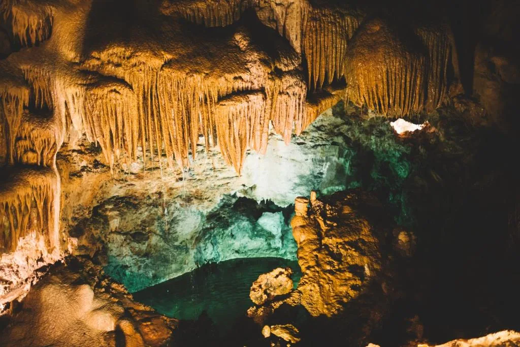Underground cave with illuminated stalactites and emerald green pool water