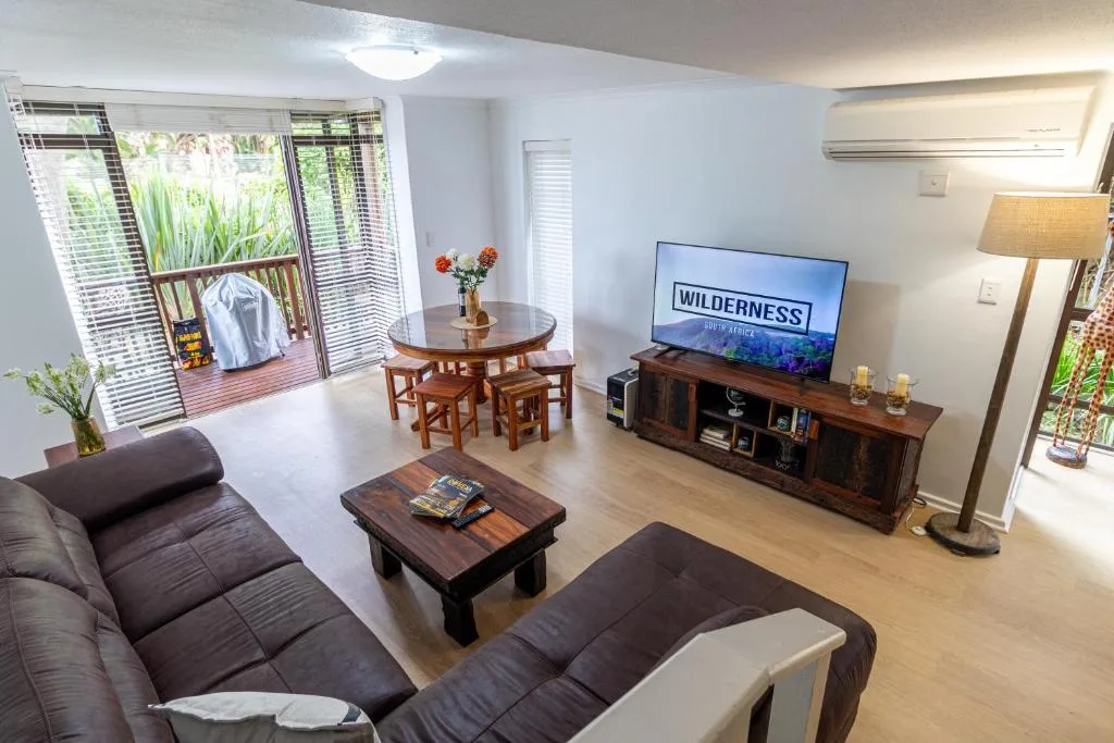 Spacious living room with dark sofas, TV, and deck access overlooking garden