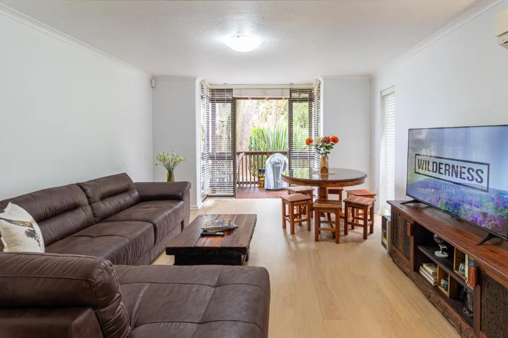 Open-plan lounge with brown leather sofa, TV, and dining area visible