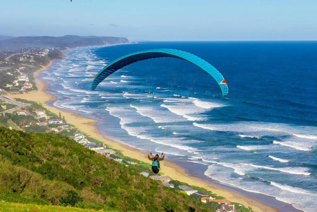 Spectacular coastal vista with paraglider soaring above sandy beach and turquoise ocean