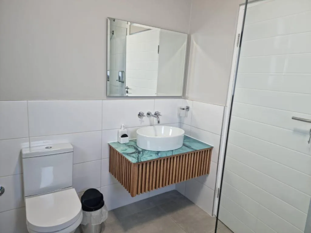 Modern bathroom with round white basin, wooden vanity, and walk-in shower