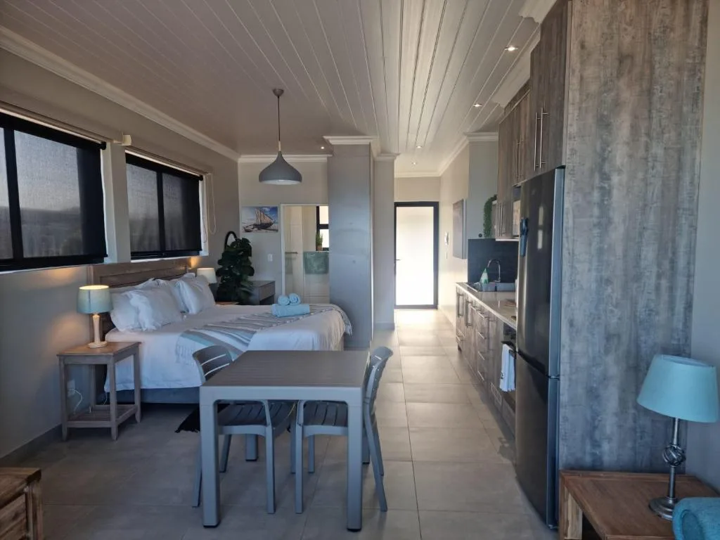 Modern bedroom with queen bed, dining table, and kitchen area visible in background