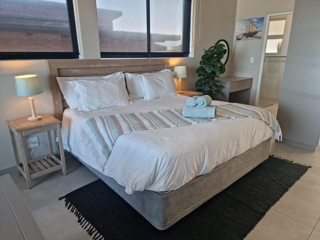 Modern bedroom with queen bed, white linens, bedside tables, and potted plant