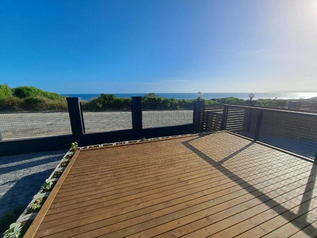 Wooden deck with ocean view, dark railings, and coastal landscape