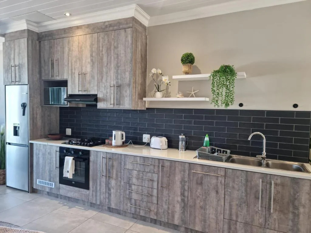 Modern kitchen with grey cabinetry, black tile backsplash, stainless steel sink and appliances