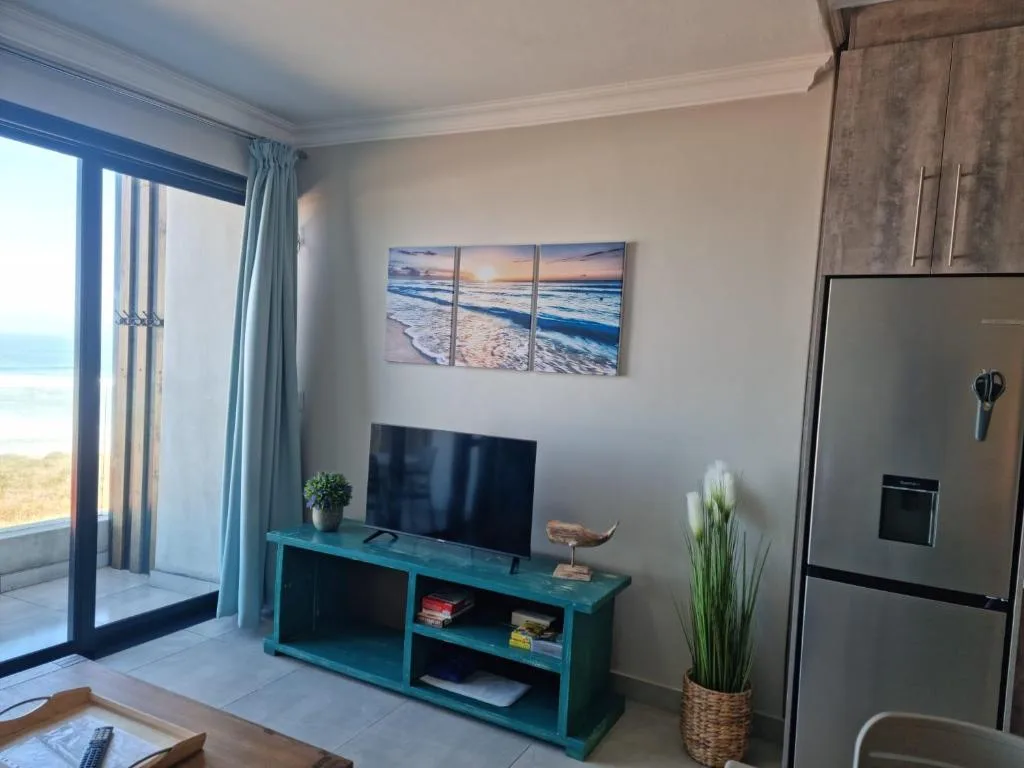 Open-plan lounge with turquoise TV unit and ocean view doors