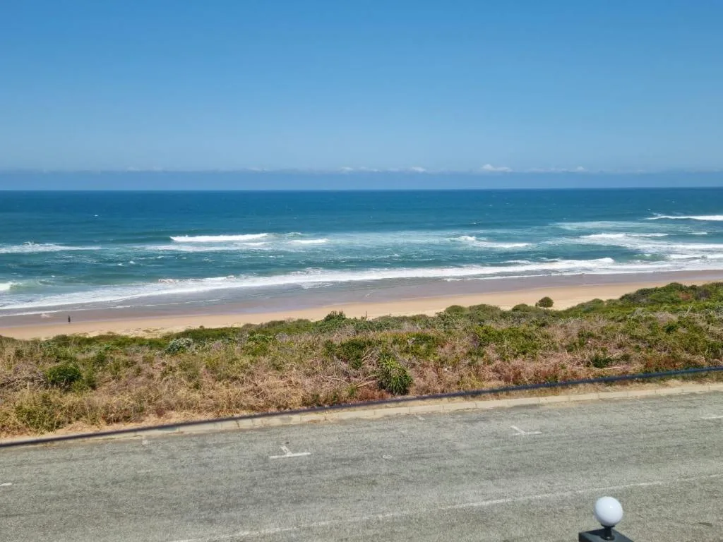 Ocean waves and sandy beach with coastal vegetation and clear blue sky