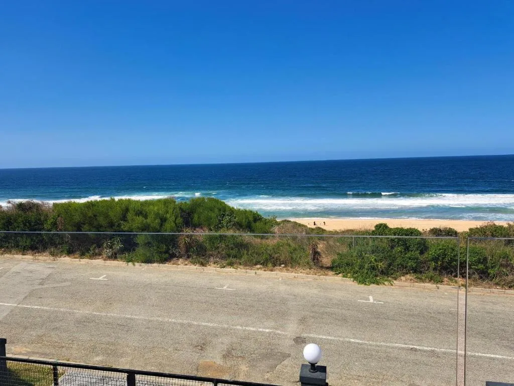 Pristine beach with waves, golden sand, and coastal vegetation under clear blue sky