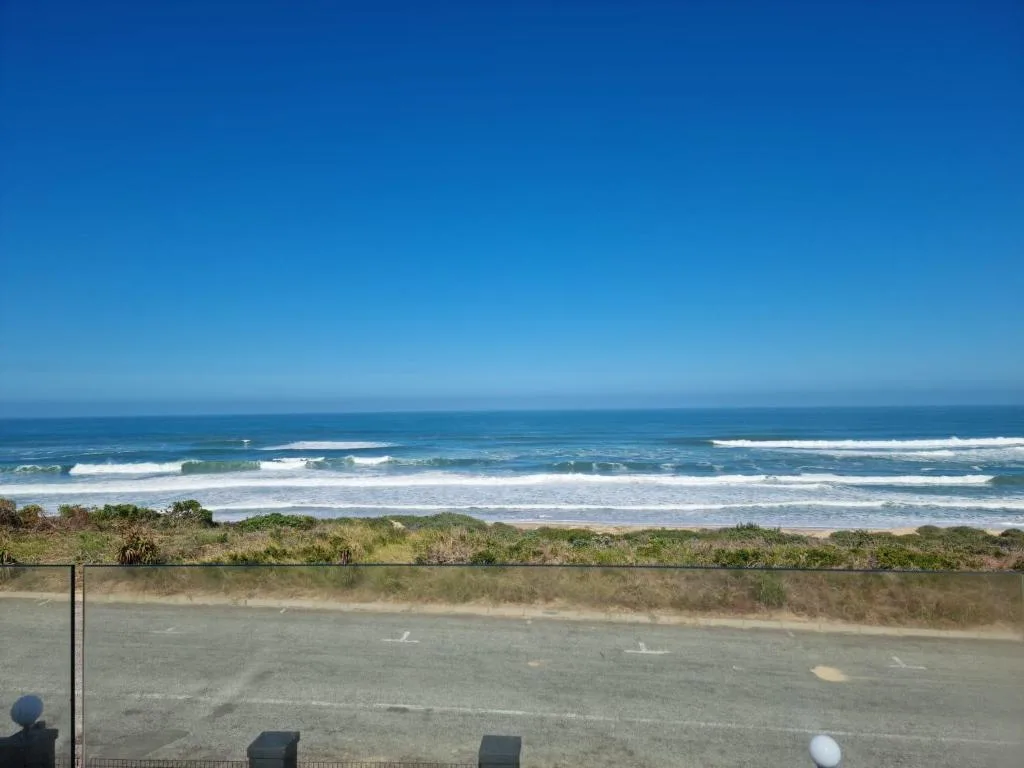Ocean waves and sandy beach stretching along the Wilderness coastline under clear blue sky