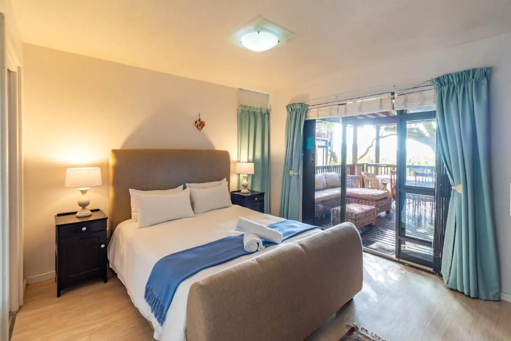 Bright bedroom with queen bed, bedside lamp, and glass doors opening to deck