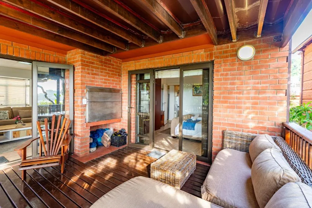 Covered brick deck with seating, fireplace, and garden views