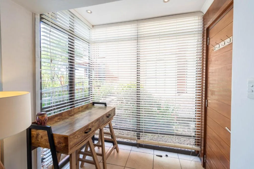 Wooden desk with lamp near bright louvered windows overlooking garden