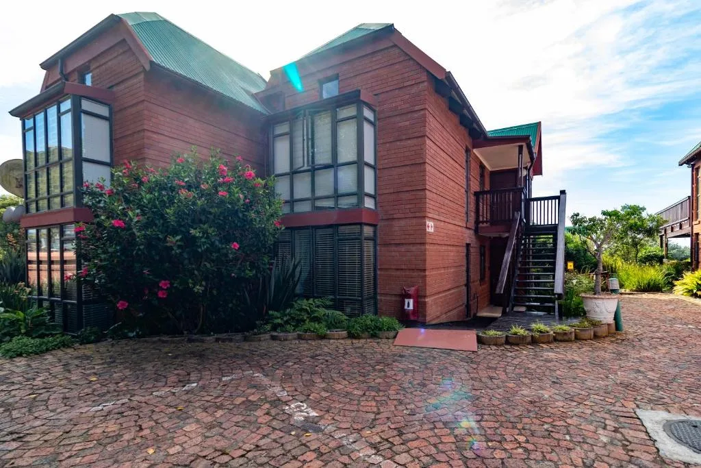 Red brick cottage with green roof and pink flowering vines climbing the facade