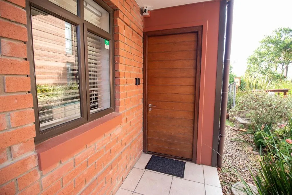 Red brick building entrance with wooden door and garden surroundings