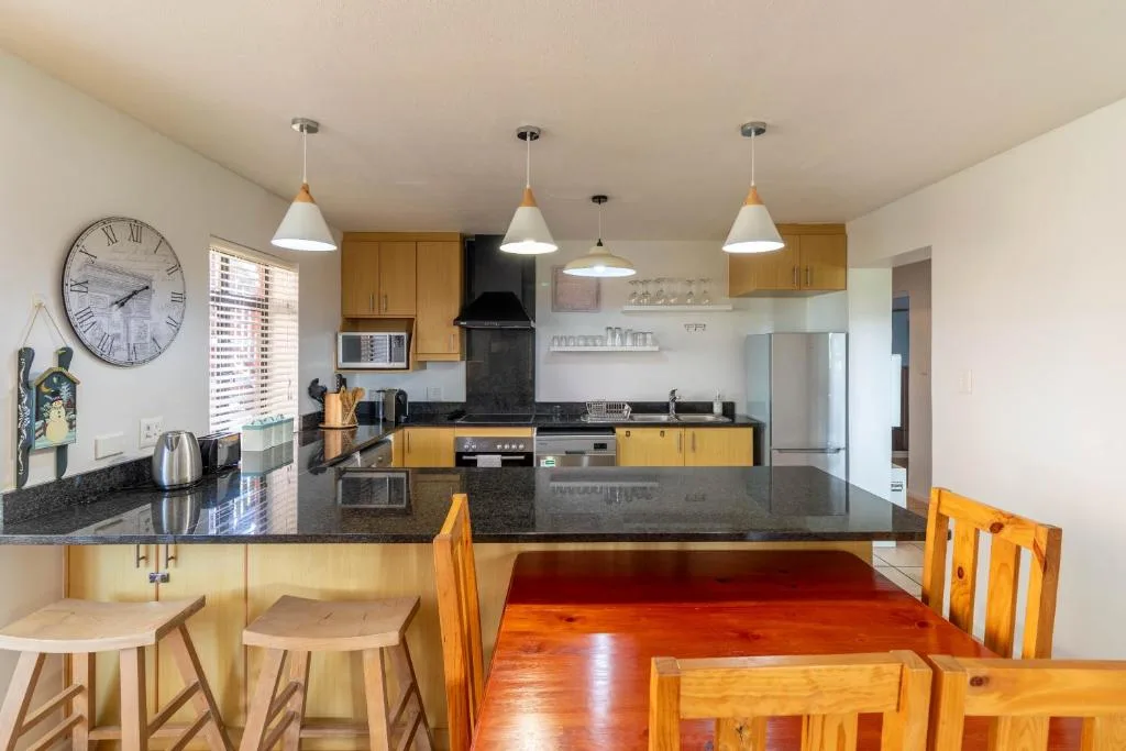 Open-plan kitchen with yellow cabinetry, black countertops, stainless steel appliances, pendant lighting