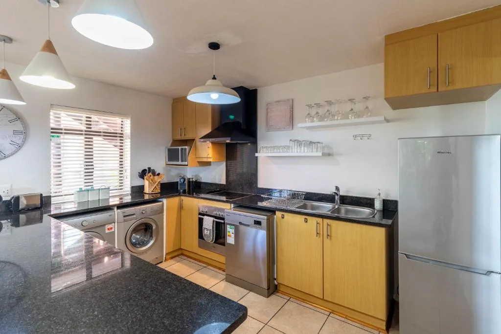 Bright modern kitchen with golden cabinetry, stainless steel appliances, and black granite counters