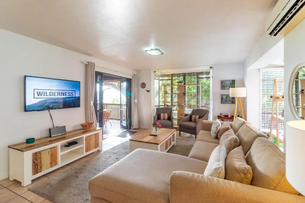 Bright lounge with cream sofa, TV, armchairs, and deck access