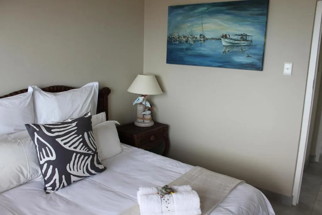 Neatly made bed with decorative pillows and coastal artwork above nightstand