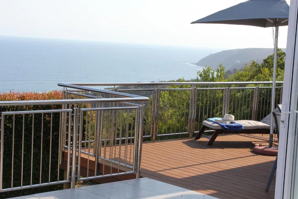 Wooden deck with ocean view, lounger, and umbrella overlooking coastal headlands